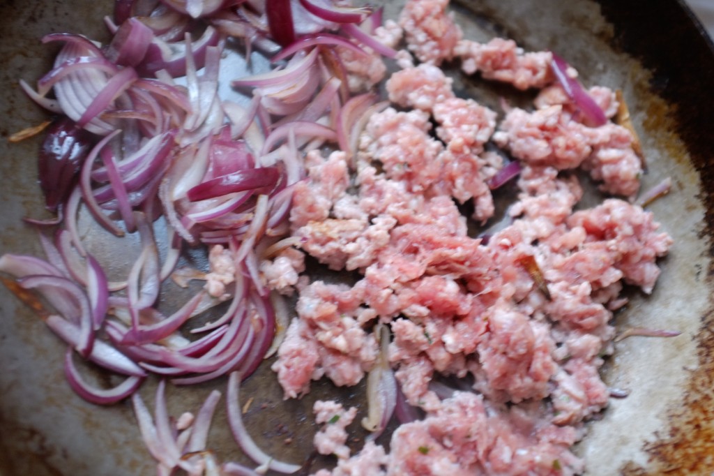 les oignons rouges et la chair à saucisse sont cuit dans une grande poêle