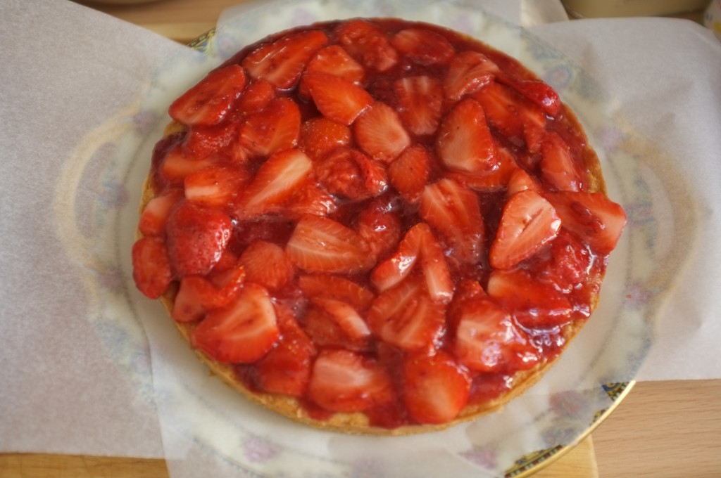 Les fraises et sirop de confiture sont déposés sur le dessus du premier gâteau. Les bords du plat de présentation sont protégés des éclaboussures par du papier cuisson.