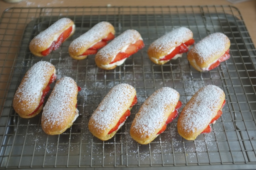 les mini éclairs sans gluten , garnis de crème fouetté et de fraises sont alors saupoudrés de sucre glace...