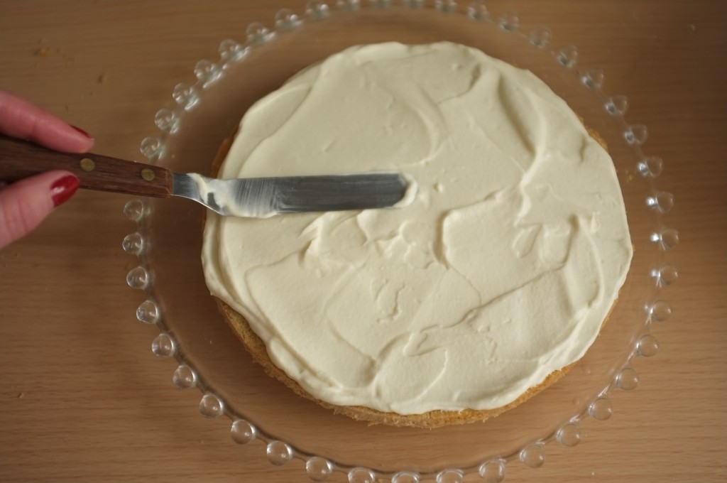 La crème chantilly maison est généreusement étalée sur le premier gâteau sans gluten