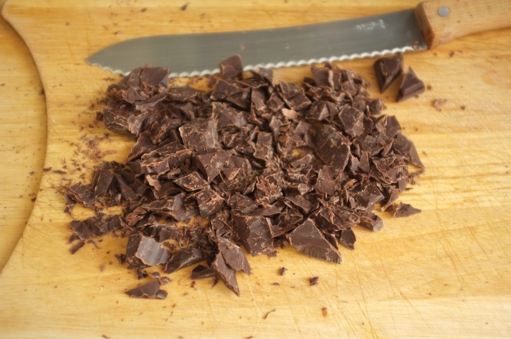 La plaque de chocolat noir pâtissier est coupé au couteau à pain en gros éclats.